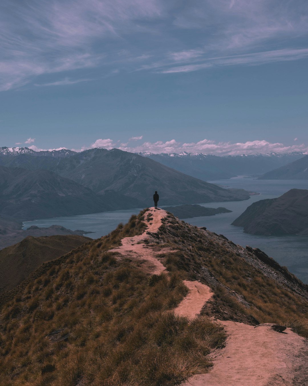 person-standing-on-cliff-near-mountain-under-cloudy-sky-during-daytime-fn-lonc3nte